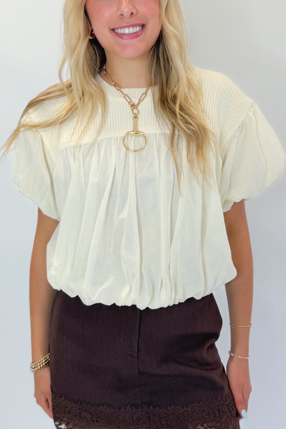 Front detail view of woman wearing Swagger Boutique’s Brown Lace Lined Denim Skort with Cream Mixed Material Bubble Hem Top against white studio background.