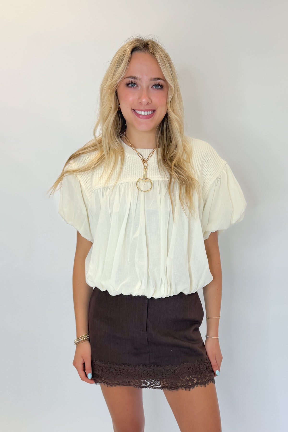 Front view of woman wearing Swagger Boutique’s Brown Lace Lined Denim Skort with Cream Mixed Material Bubble Hem Top against white studio background.