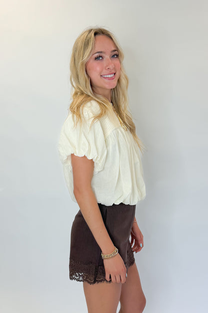 Side view of woman wearing Swagger Boutique’s Brown Lace Lined Denim Skort with Cream Mixed Material Bubble Hem Top against white studio background.