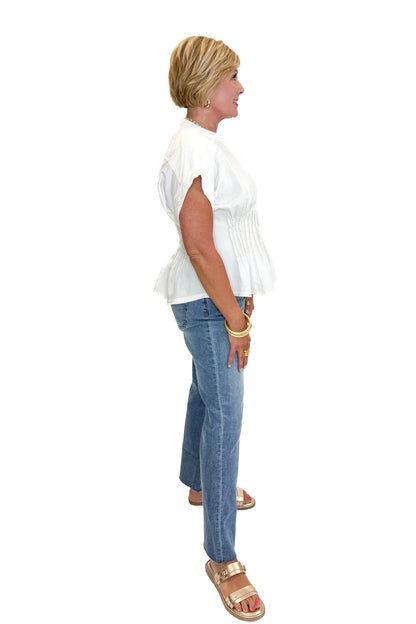 Side view of woman wearing Swagger Boutique’s Cream Pintuck Waist Top with jeans against white studio background.