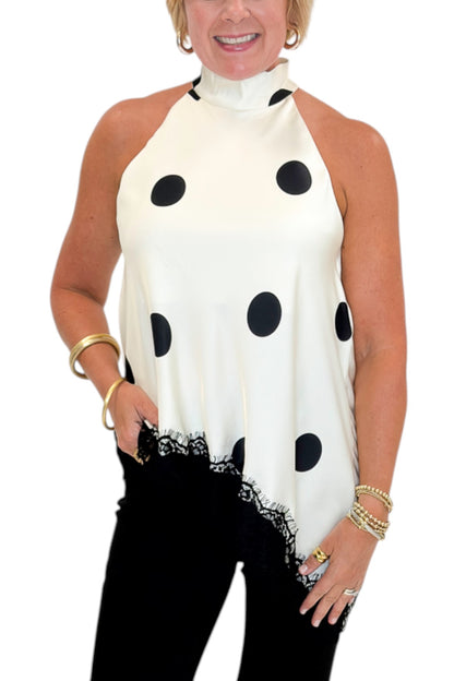 Front detail view of woman wearing Swagger Boutique’s Cream Polka Dot Asymmetrical Halter Neck Satin Lace Top by Entro with jeans against white studio background.