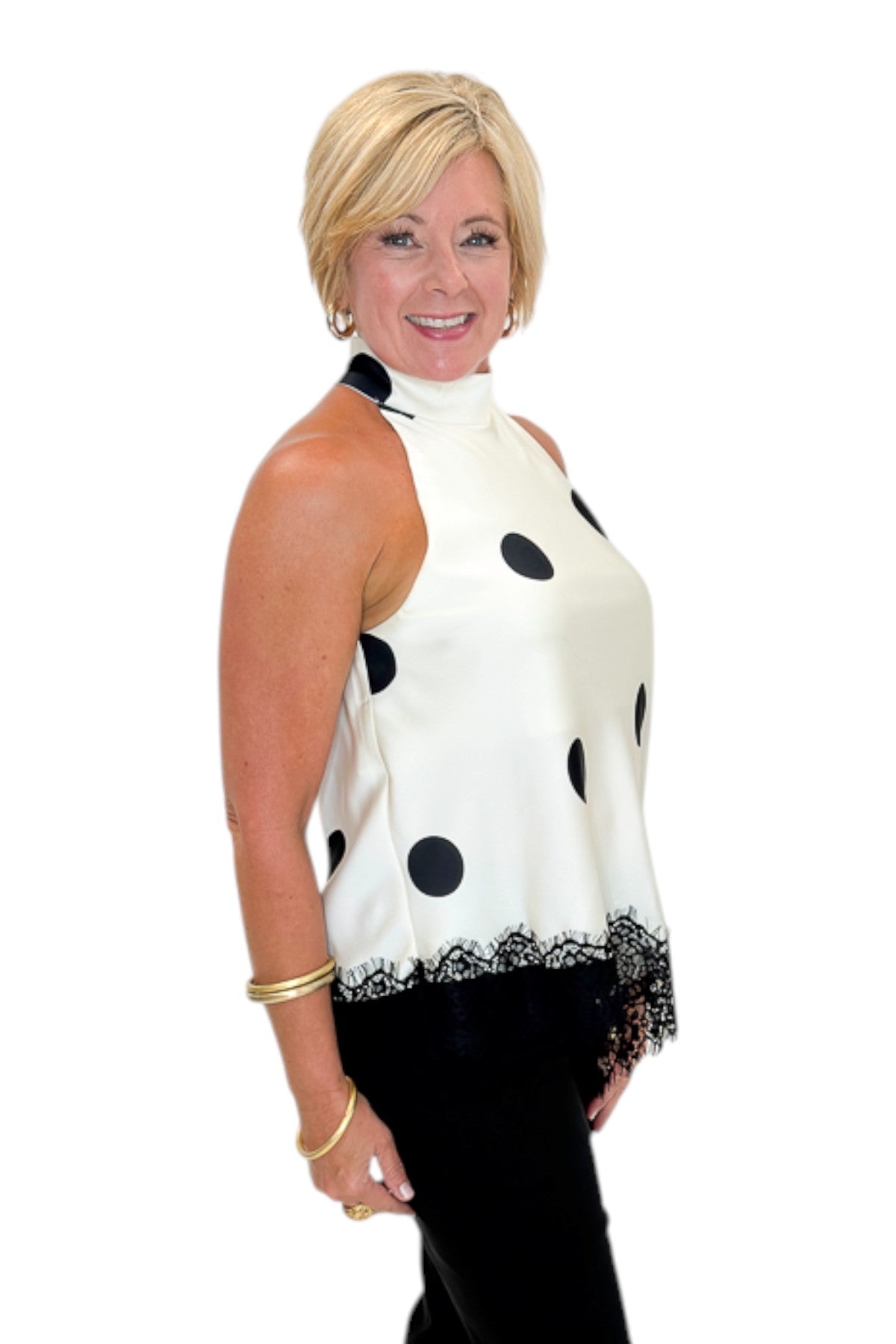Side view of woman wearing Swagger Boutique’s Cream Polka Dot Asymmetrical Halter Neck Satin Lace Top by Entro with jeans against white studio background.