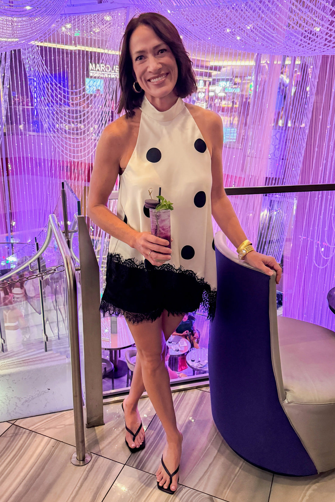 Front view of woman wearing Swagger Boutique’s lace trim halter top with Black Lace Hem Shorts by Entro standing at a restaurant and bar.