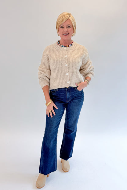 Front view of woman wearing Swagger Boutique’s Cream Ribbed Button Up Cardigan with jeans against white studio background.