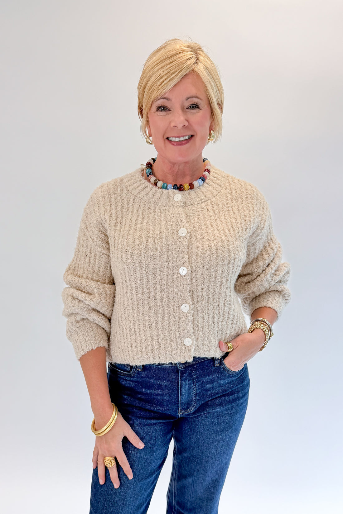 Front view of woman wearing Swagger Boutique’s Cream Ribbed Button Up Cardigan with jeans against white studio background.