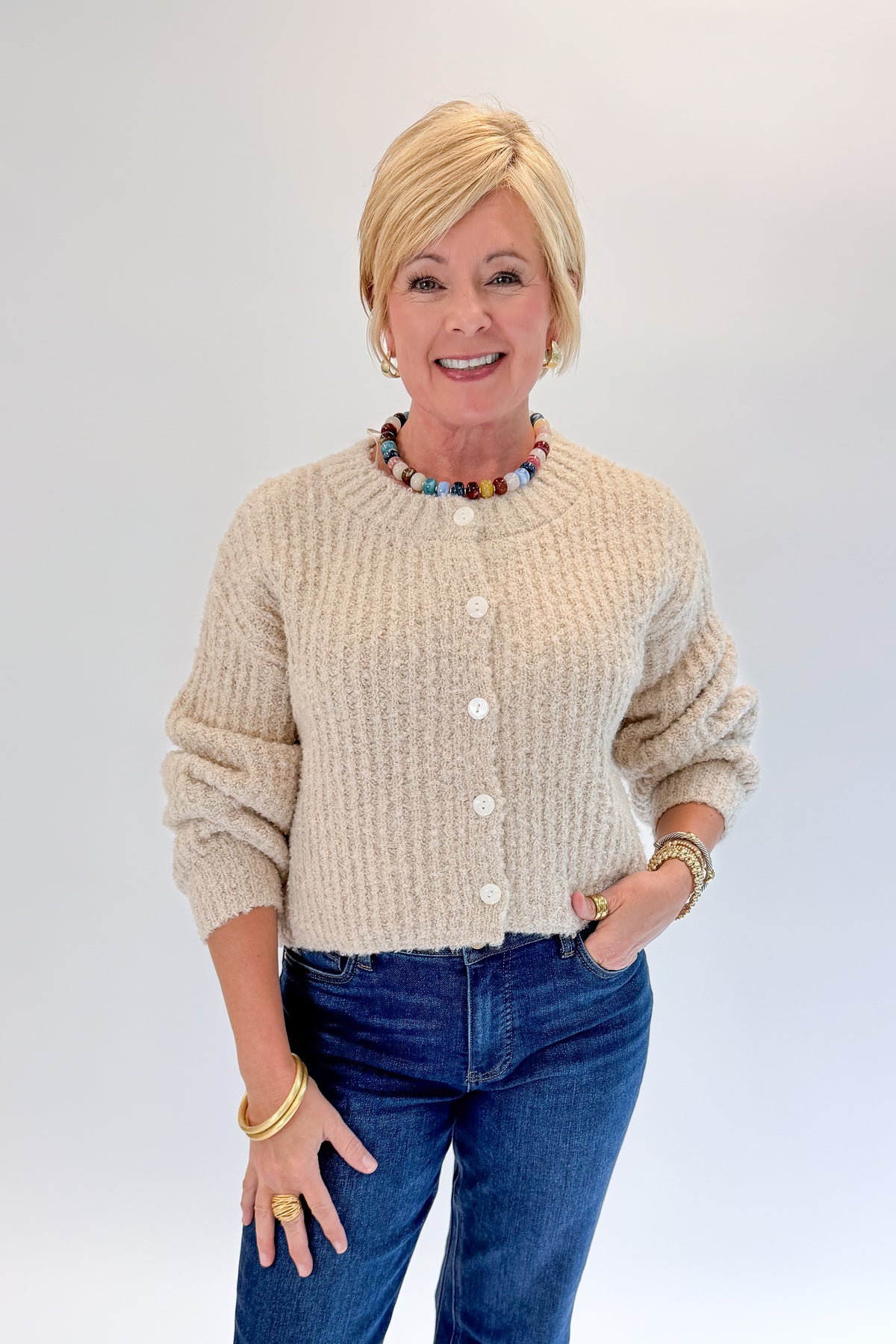 Front view of woman wearing Swagger Boutique’s Cream Ribbed Button Up Cardigan with jeans against white studio background.