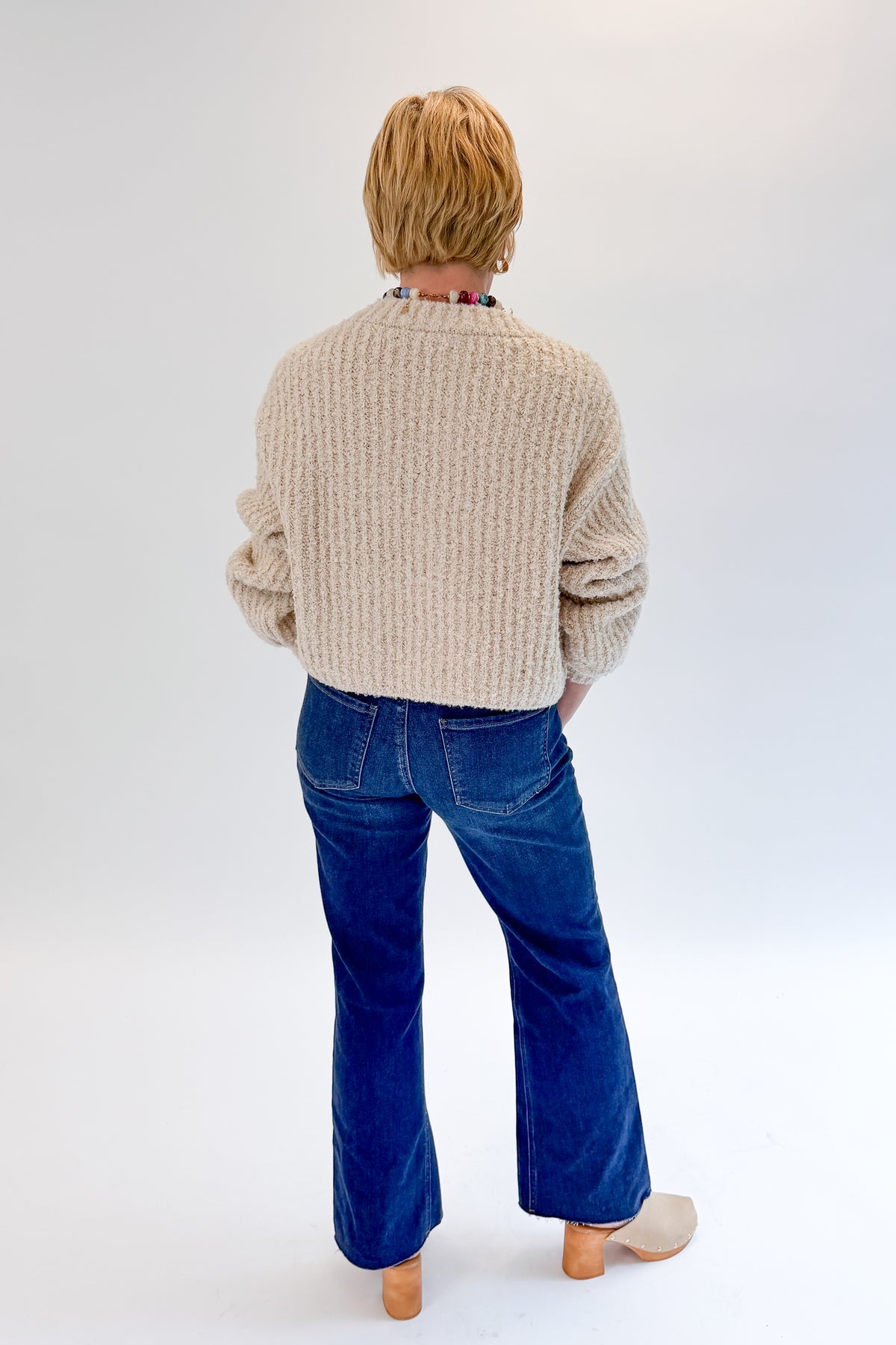 Back view of woman wearing Swagger Boutique’s Cream Ribbed Button Up Cardigan with jeans against white studio background.