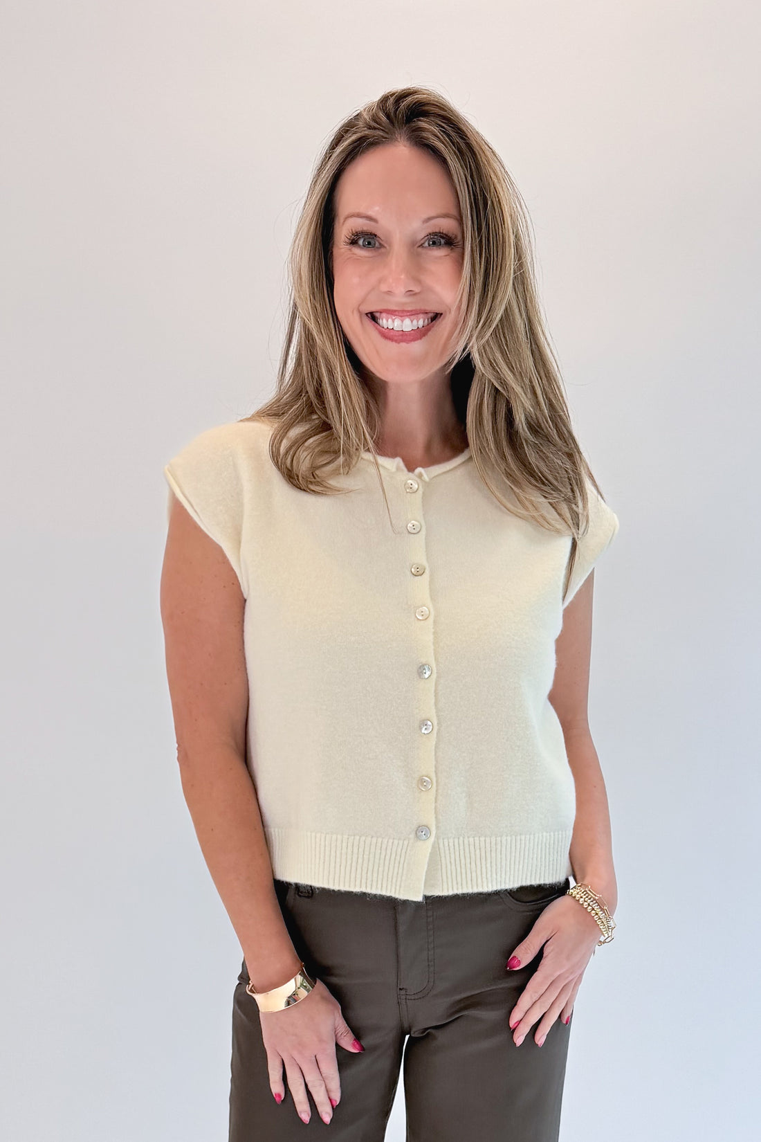 Front view of woman wearing Swagger Boutique’s Cream Sleeveless Button Up Sweater with Jeans against white studio background.