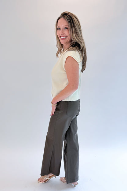 Side view of woman wearing Swagger Boutique’s Cream Sleeveless Button Up Sweater with Jeans against white studio background.