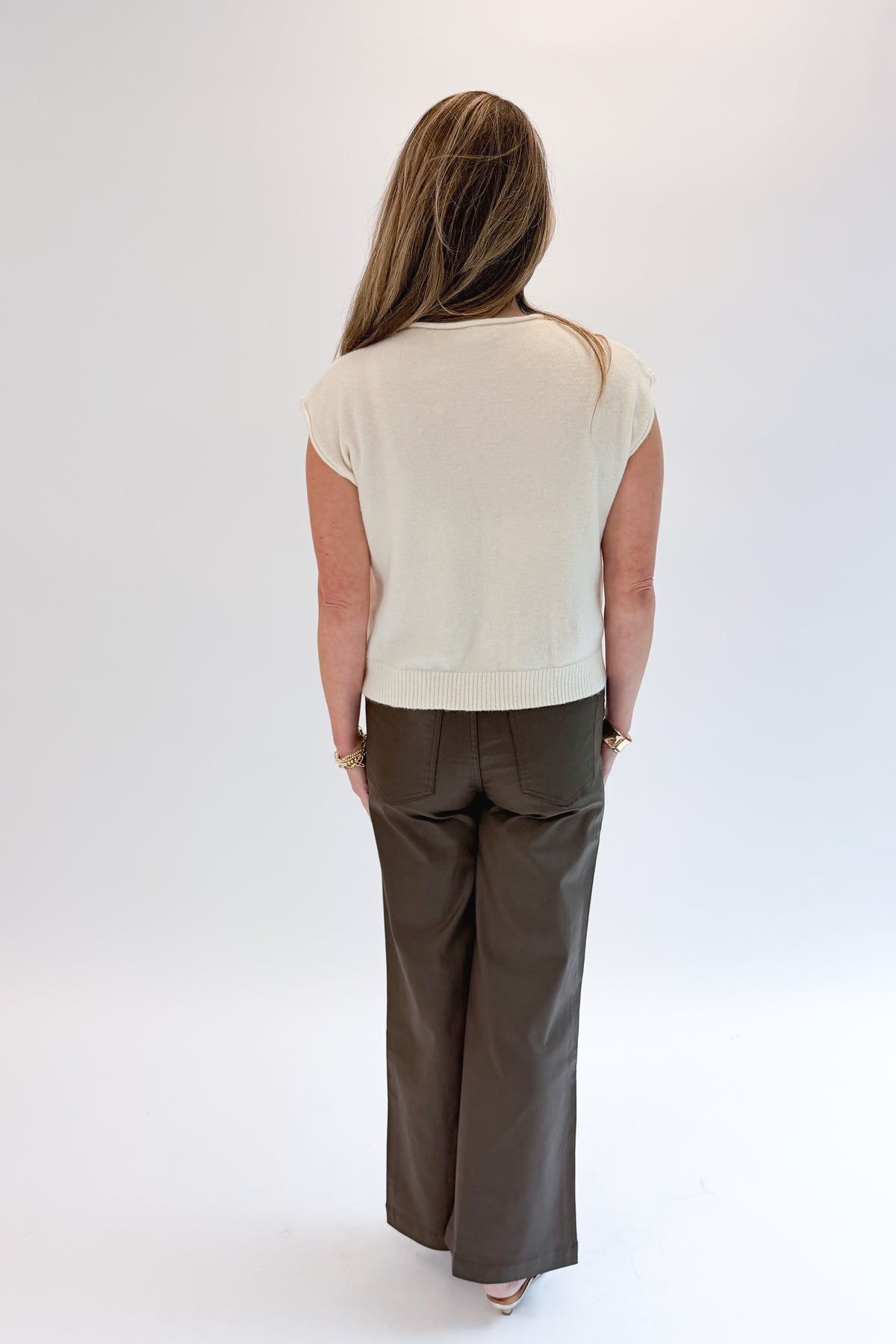 Back view of woman wearing Swagger Boutique’s Cream Sleeveless Button Up Sweater with Jeans against white studio background.