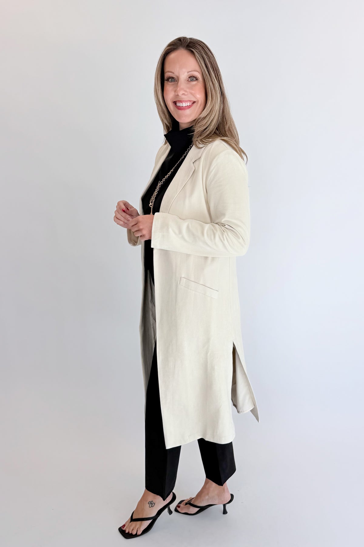 Side view of woman wearing Swagger Boutique’s Cream Suede Duster Cardigan with jeans against white studio background.
