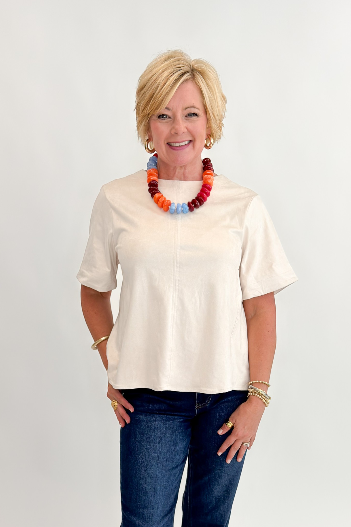 Front view of woman wearing Swagger Boutique’s Cream Suede Swing Top with jeans against white studio background.