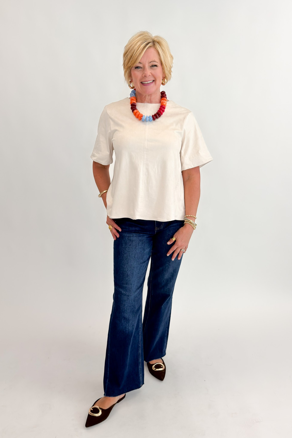 Front view of woman wearing Swagger Boutique’s Cream Suede Swing Top with jeans against white studio background.