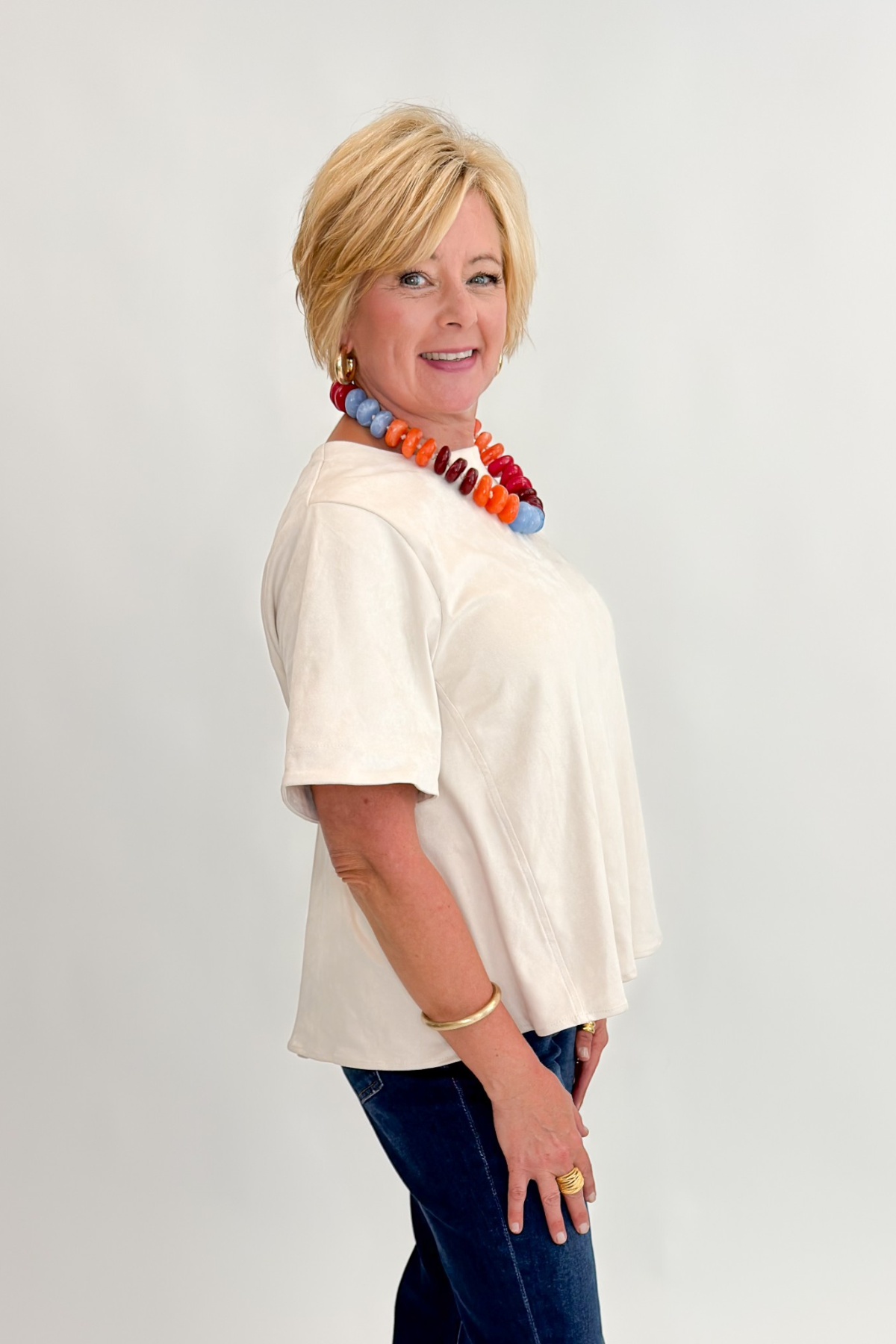 Side view of woman wearing Swagger Boutique’s Cream Suede Swing Top with jeans against white studio background.