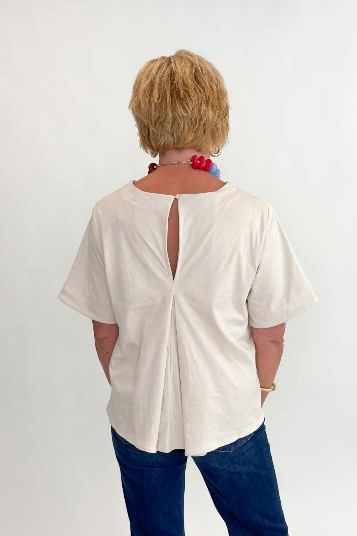 Back view of woman wearing Swagger Boutique’s Cream Suede Swing Top with jeans against white studio background.