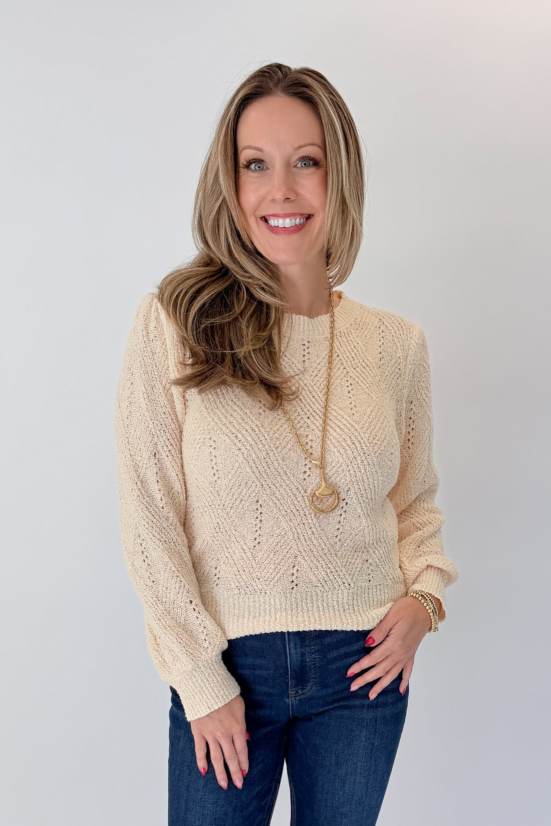 Front view of woman wearing Swagger Boutique’s Cream Textured Crew Neck Sweater with jeans against white studio background.