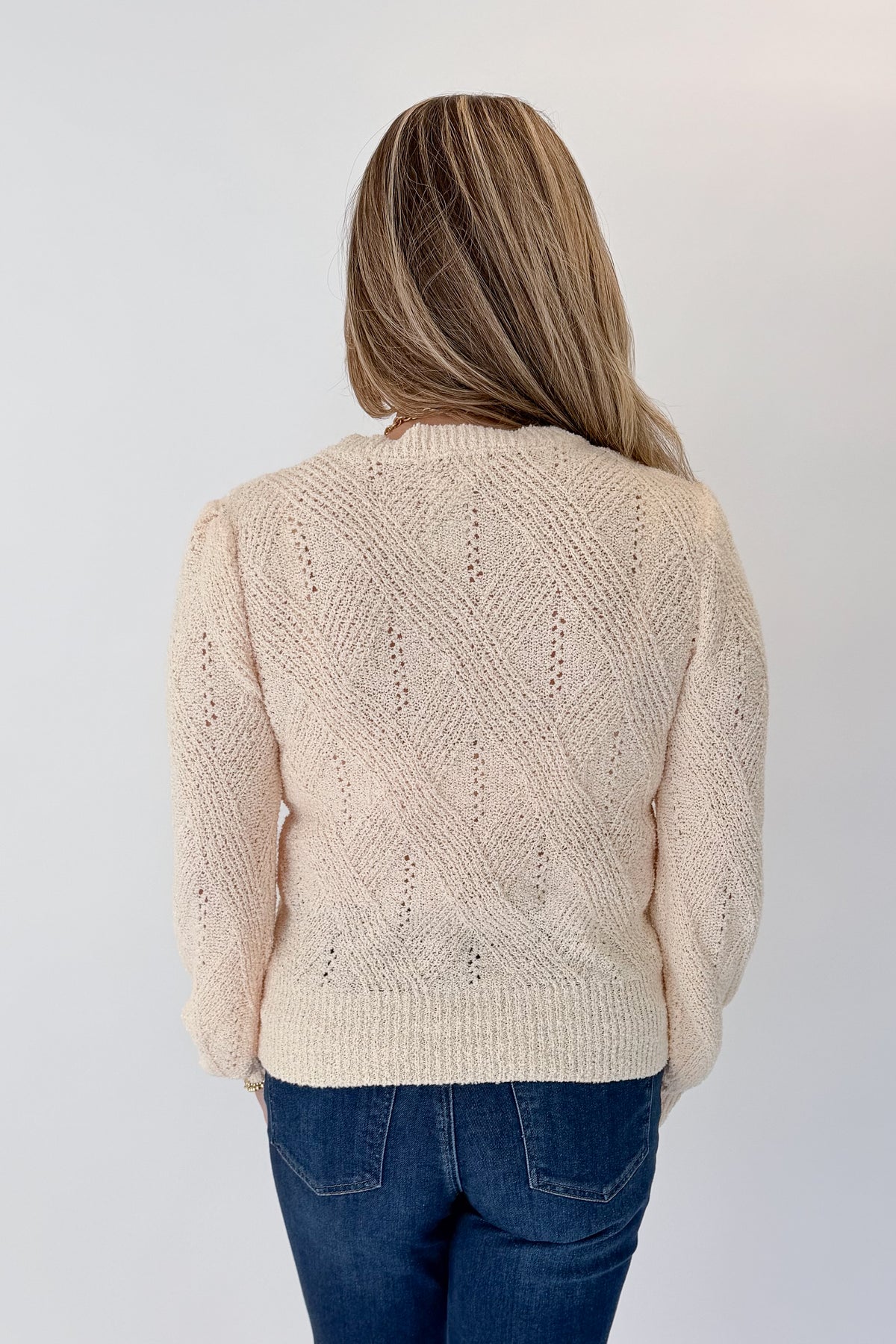 Back view of woman wearing Swagger Boutique’s Cream Textured Crew Neck Sweater with jeans against white studio background.