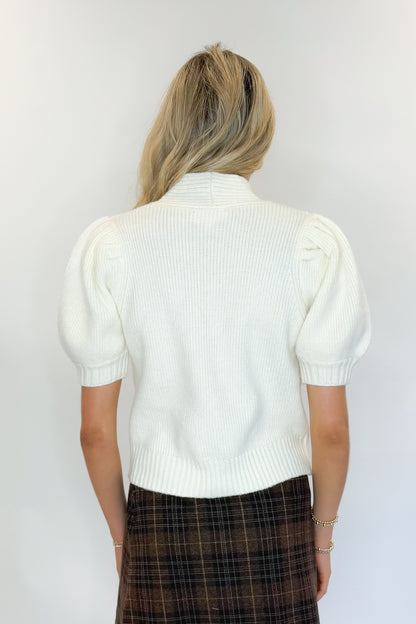 Back view of woman wearing Swagger Boutique’s Cream Tie Neck Short Sleeve Sweater by Entro with Brown Plaid Mini Skirt against white studio background.
