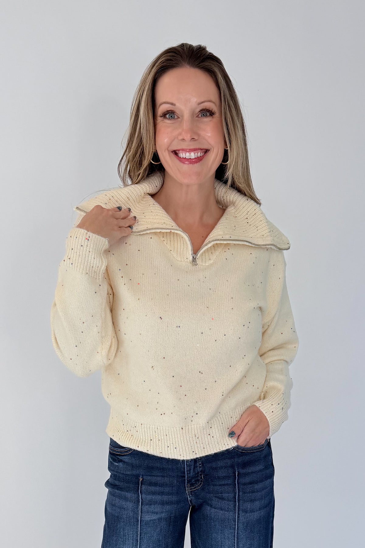 Front view of woman wearing Swagger Boutique’s Cream With Multi Sequins Sweater with jeans against white studio background.