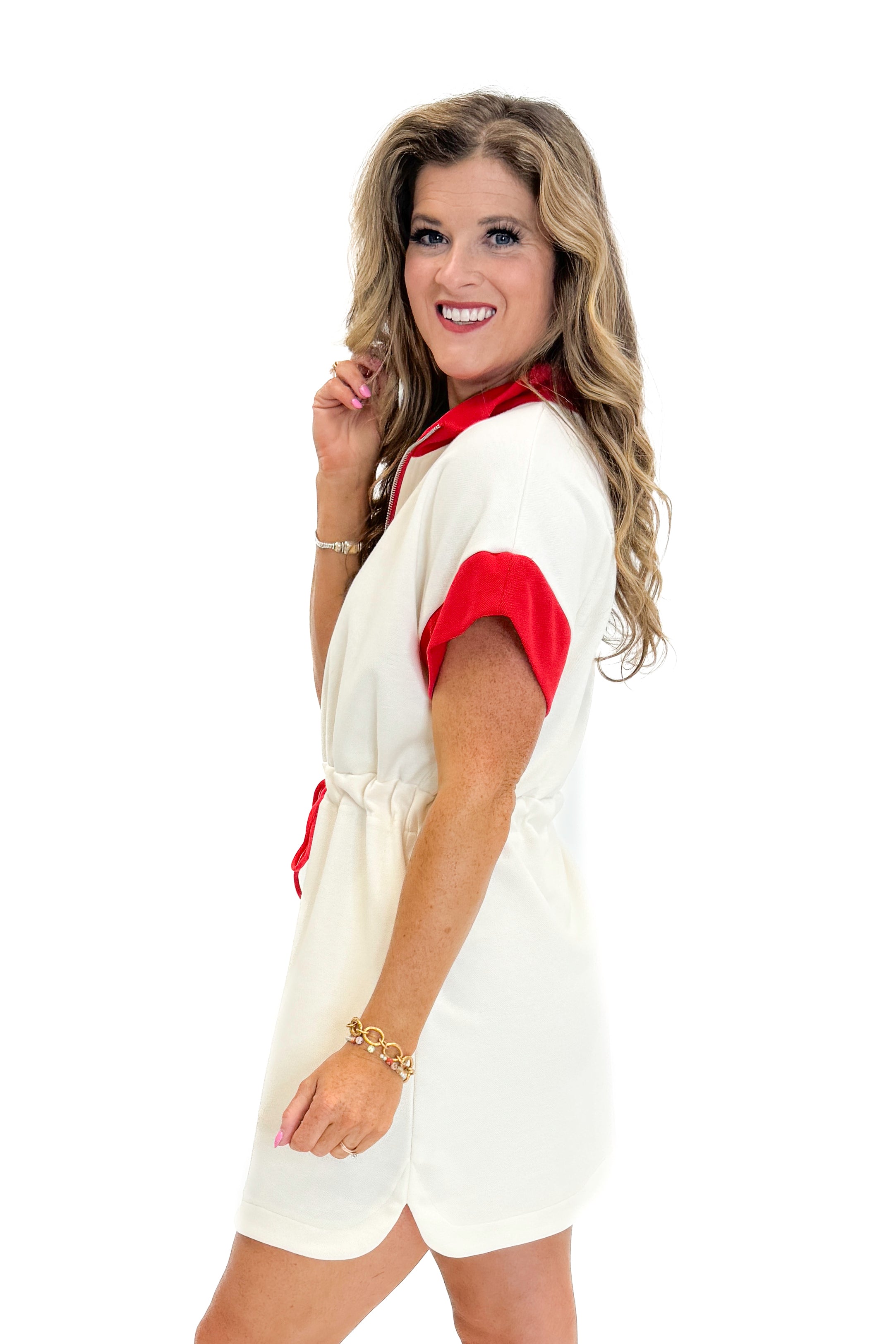 Side view of woman wearing Swagger Boutique’s Cream With Red Accent Drawstring Dress with sneakers against white studio background.
