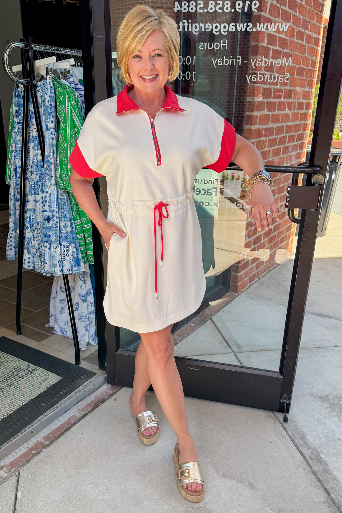 Front view of woman wearing Swagger Boutique’s Cream With Red Accent Drawstring Dress with sandals standing outside the store.