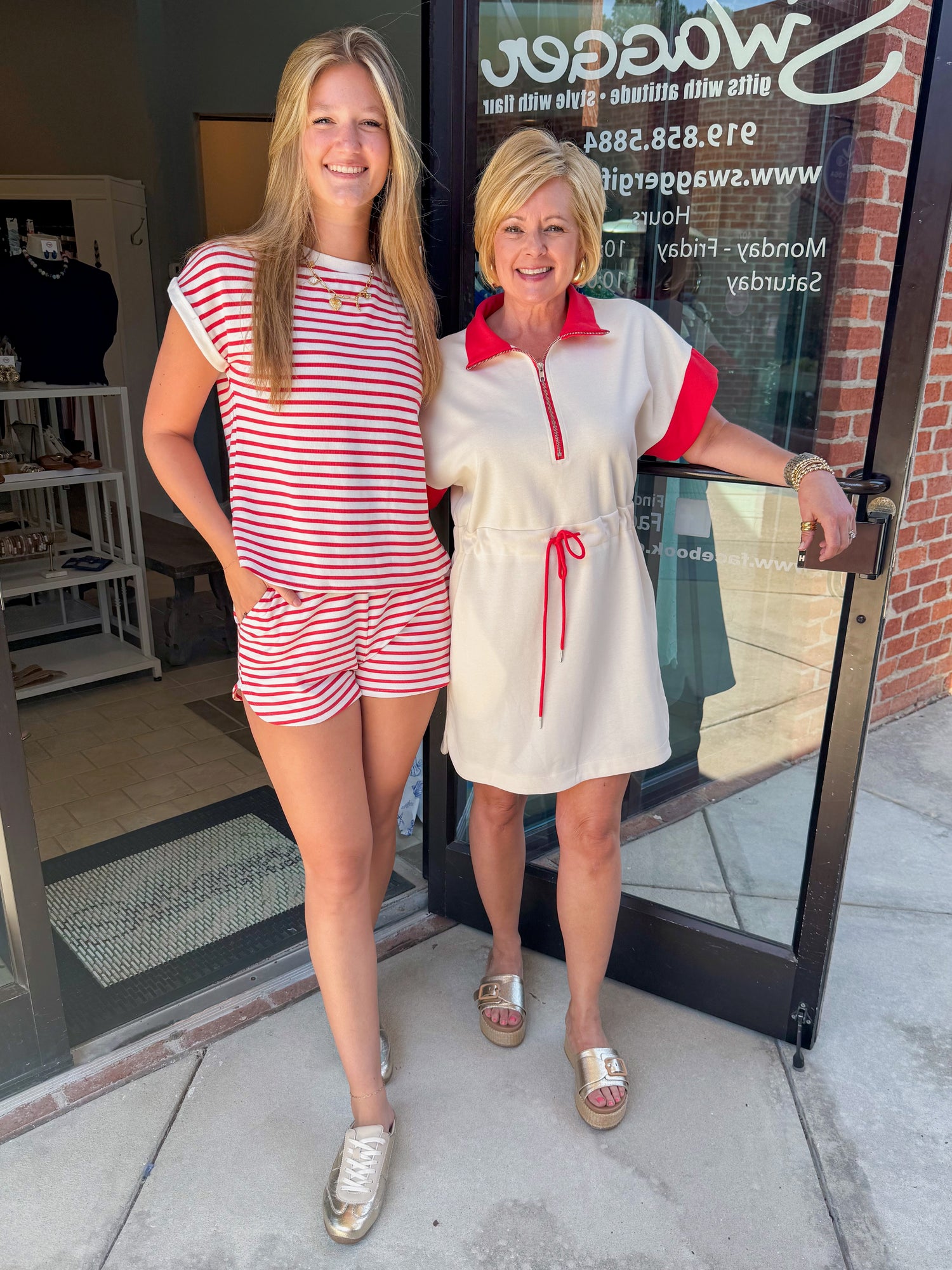 Front view of woman wearing Swagger Boutique’s Cream With Red Accent Drawstring Dress and woman wearing red & white stripe set standing outside the store.