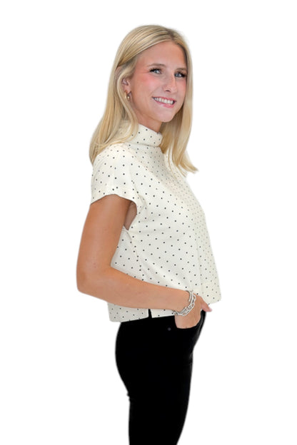 Side view of woman wearing Swagger Boutique’s Cream &amp; Black Polka Dot Mock Neck Top by Entro with jeans against white studio background.