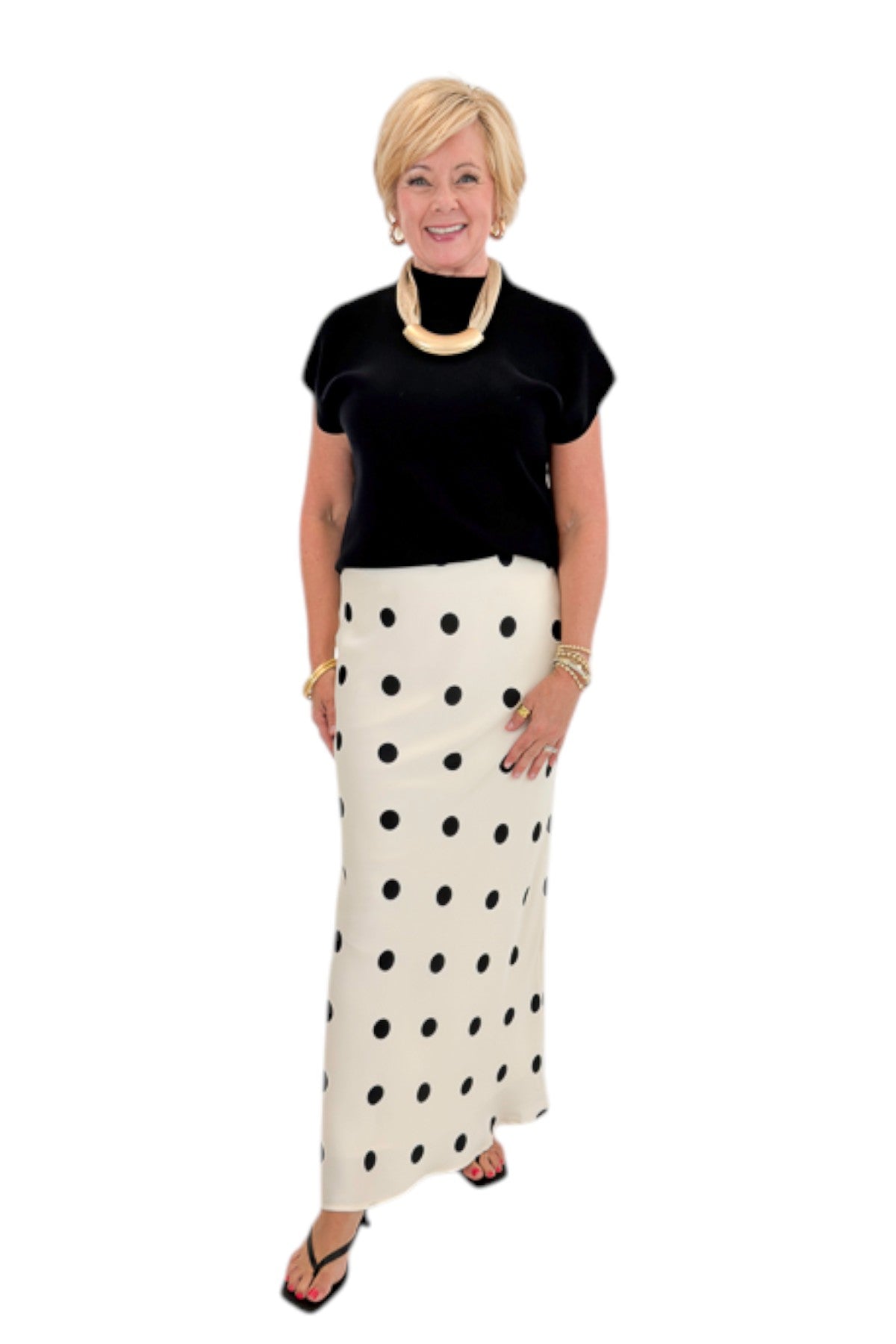 Front view of woman wearing Swagger Boutique’s Black Shirred Cap Sleeve Sweater with Cream &amp; Black Polka Dot Satin Skirt against white studio background.