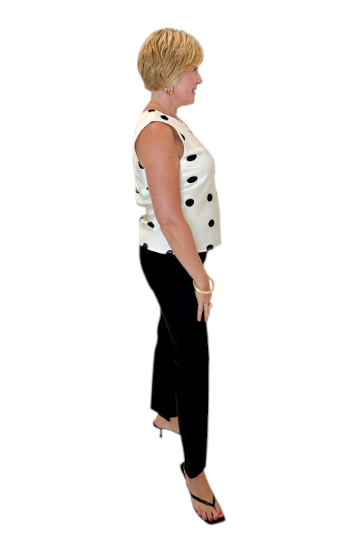 Side view of woman wearing Swagger Boutique’s Cream &amp; Black Polka Dot Satin Tank with jeans against white studio background.