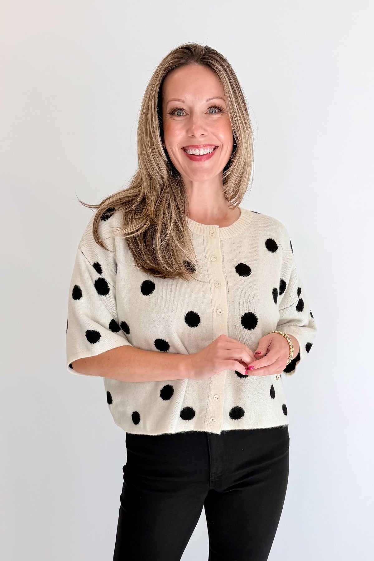 Front view of woman wearing Swagger Boutique’s Cream &amp; Black Polka Dot Short Sleeve Cardigan with jeans against white studio background.