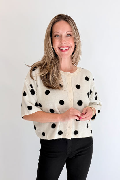 Front view of woman wearing Swagger Boutique’s Cream &amp; Black Polka Dot Short Sleeve Cardigan with jeans against white studio background.