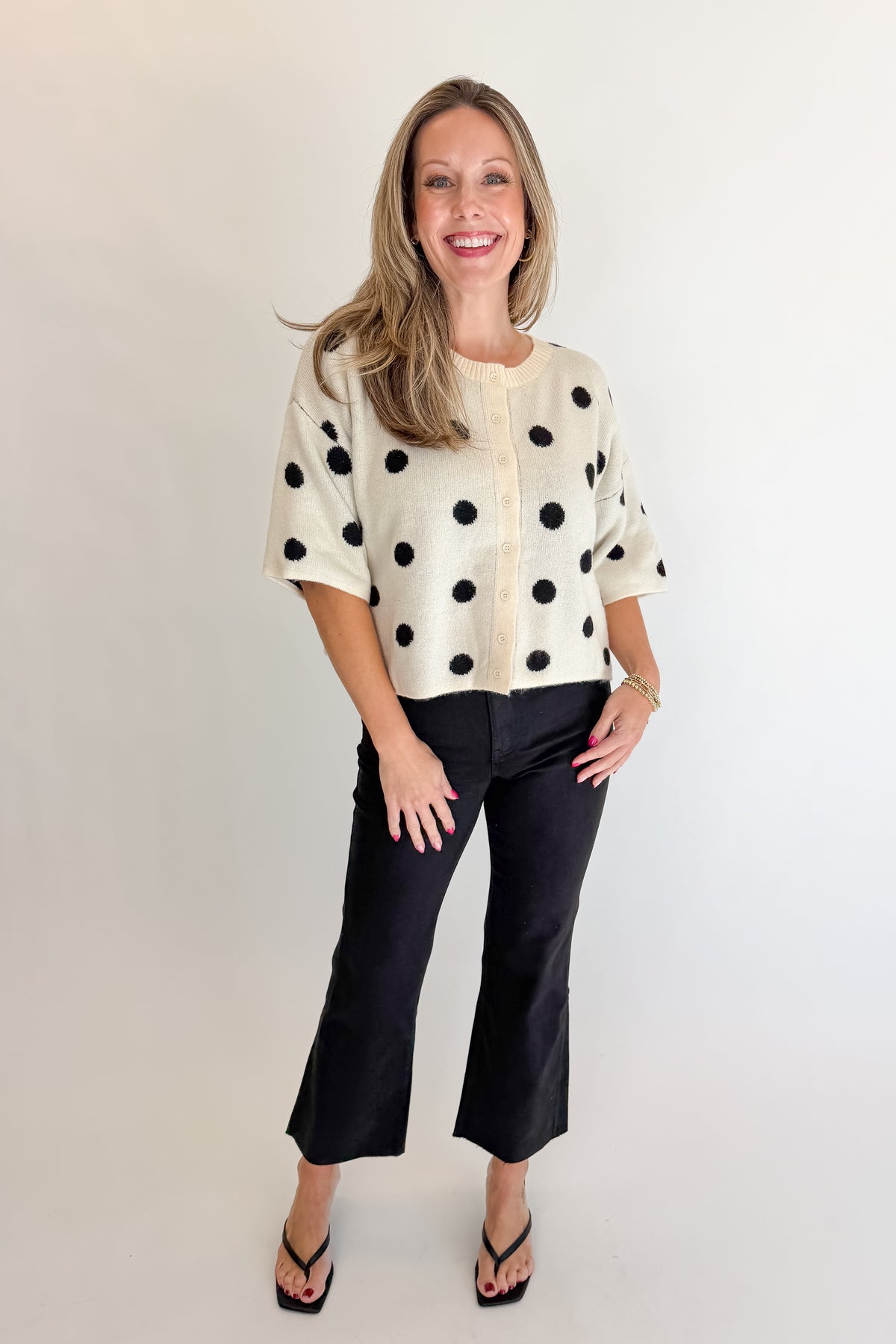 Front view of woman wearing Swagger Boutique’s Cream &amp; Black Polka Dot Short Sleeve Cardigan with jeans against white studio background.