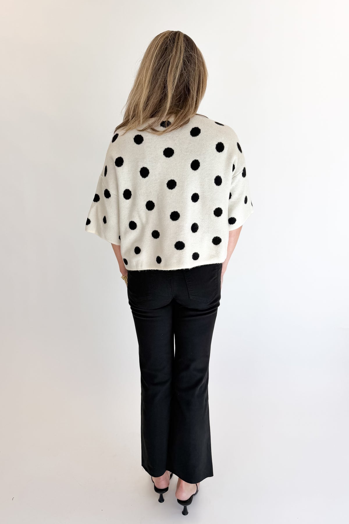 Back view of woman wearing Swagger Boutique’s Cream &amp; Black Polka Dot Short Sleeve Cardigan with jeans against white studio background.
