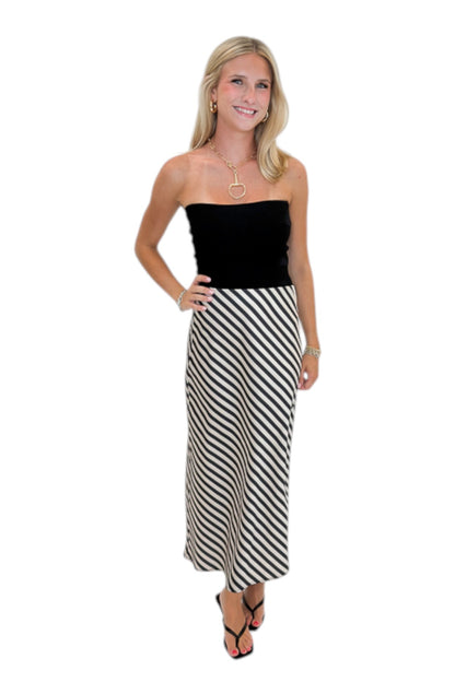 Front view of woman wearing Swagger Boutique’s Cream &amp; Black Striped Satin Midi Skirt with black top against white studio background.