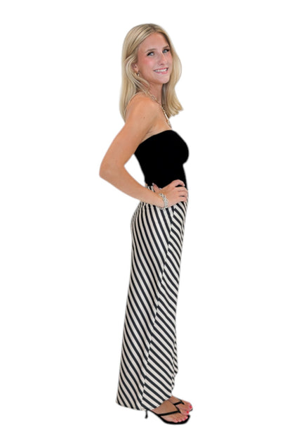 Side view of woman wearing Swagger Boutique’s Cream &amp; Black Striped Satin Midi Skirt with black top against white studio background.