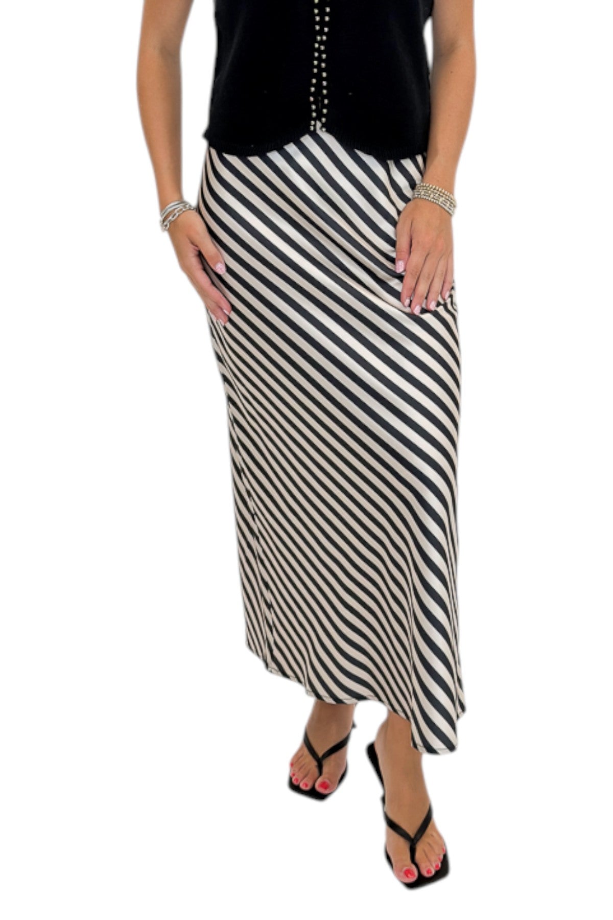 Front detail view of woman wearing Swagger Boutique’s Cream &amp; Black Striped Satin Midi Skirt with black top against white studio background.