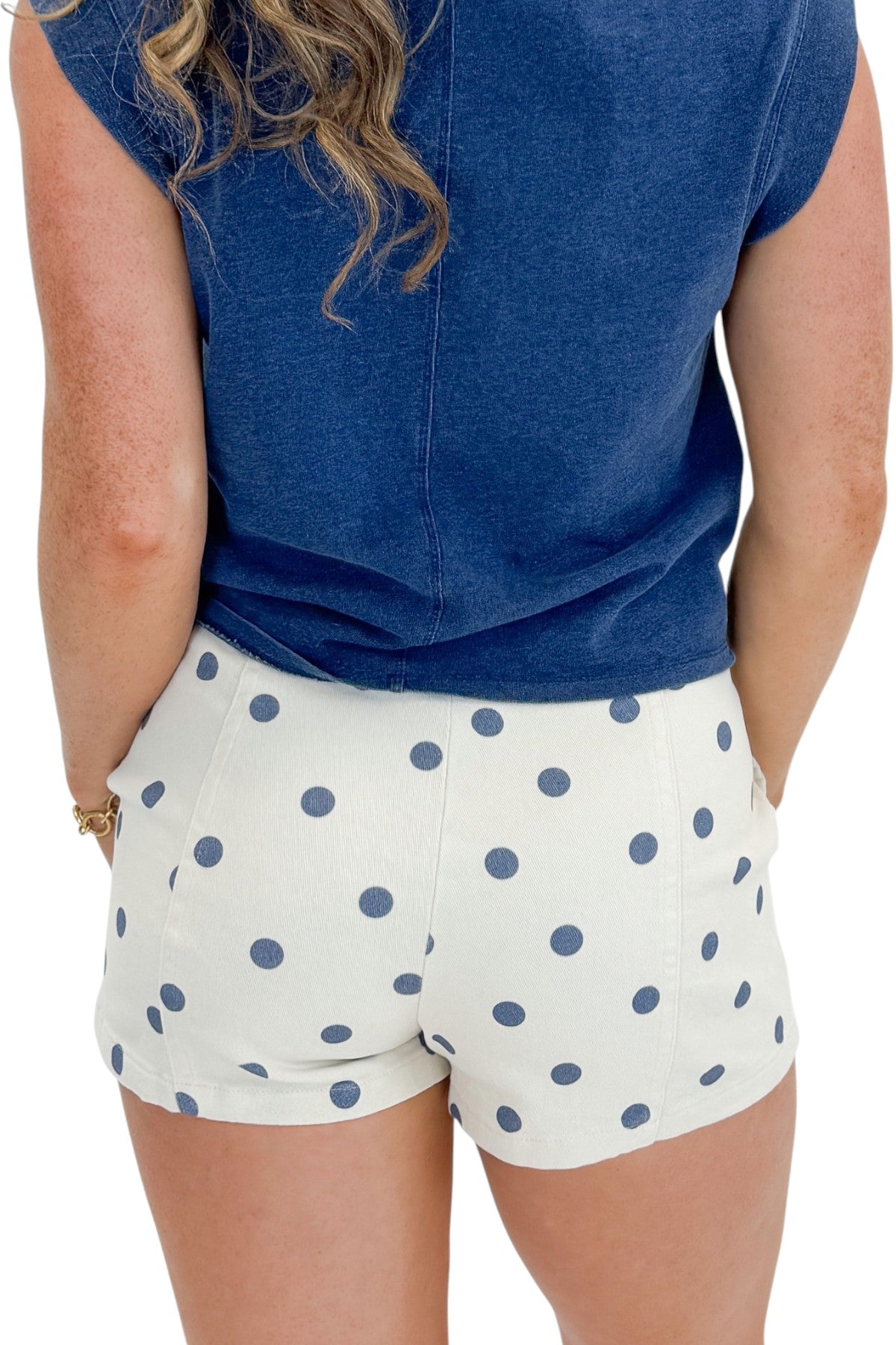 Back detail view of woman wearing Swagger Boutique’s Cream &amp; Blue Polka Dot Shorts with Z Supply Camino top with clothing hanging in the background.