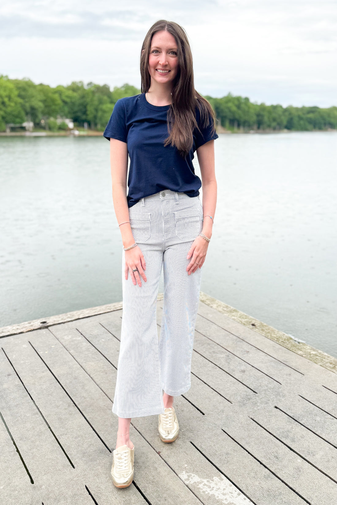 Front view of woman wearing Swagger Boutique’s Cream &amp; Blue Striped Jeans With Patch Pocket by Just Black Denim with blue Z Supply top outside at a lake.