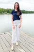 Front view of woman wearing Swagger Boutique’s Cream & Blue Striped Jeans With Patch Pocket by Just Black Denim with blue Z Supply top outside at a lake.
