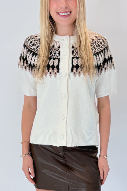 Front detail view of woman wearing Swagger Boutique’s Cream &amp; Brown Fair Isle Button Up Short Sleeve Sweater with brown faux leather mini skirt against white studio background. 