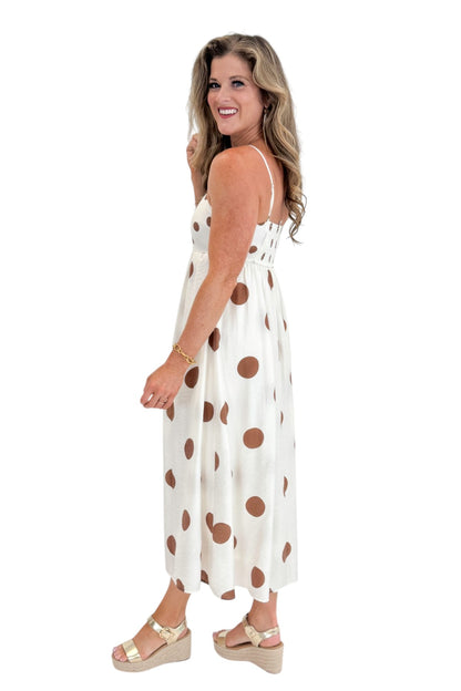 Side view of woman wearing Swagger Boutique’s Cream &amp; Brown Polka Dot Midi Dress with sandals against white studio background.