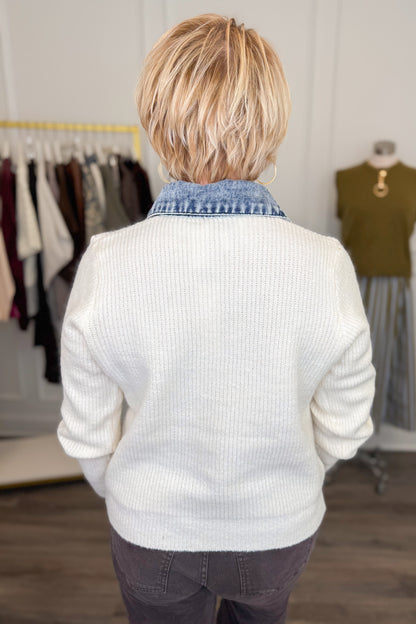 Back view of woman wearing Swagger Boutique’s Cream &amp; Denim Collared Button Up Sweater with Kelsey Coated Ankle Flare Jeans in Chocolate by Kut from the Kloth with clothing hanging in the background.