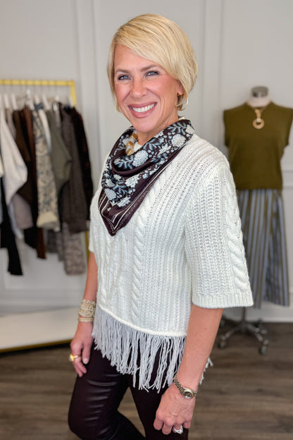 Side view of woman wearing Swagger Boutique’s Cream Fringe Short Sleeve Sweater with jeans with clothing hanging in the background.