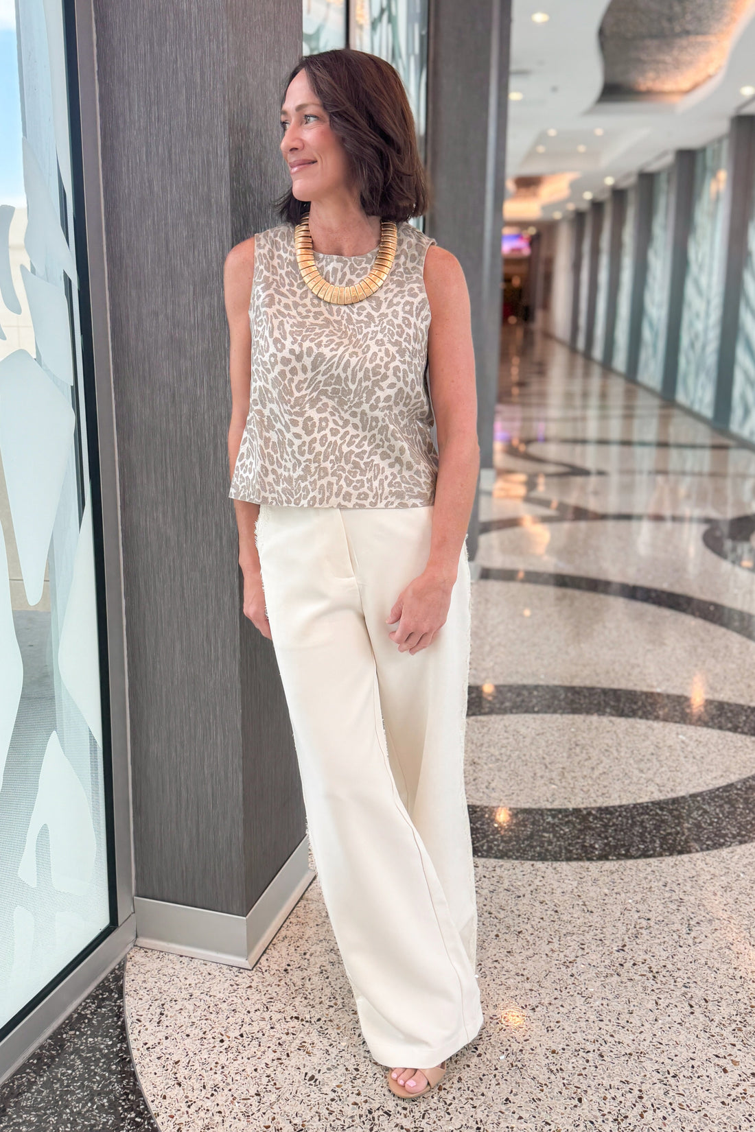 Front detail view of woman wearing Swagger Boutique’s Cream Lace Lined Pants with Metallic leopard print tank standing in a building hallway.