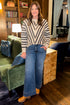 Front view of woman wearing Swagger Boutique’s Cream & Navy Chevron Sweater with jeans standing in a lounge.