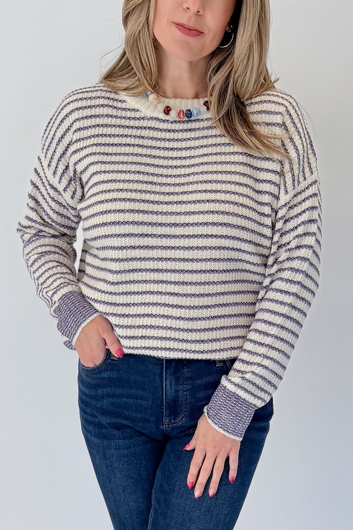Front detail view of woman wearing Swagger Boutique’s Cream &amp; Purple Striped Sweater with jeans against white studio background.