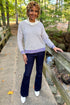 Front view of woman wearing Swagger Boutique’s Cream & Purple Striped Sweater with jeans standing on a bridge outside.