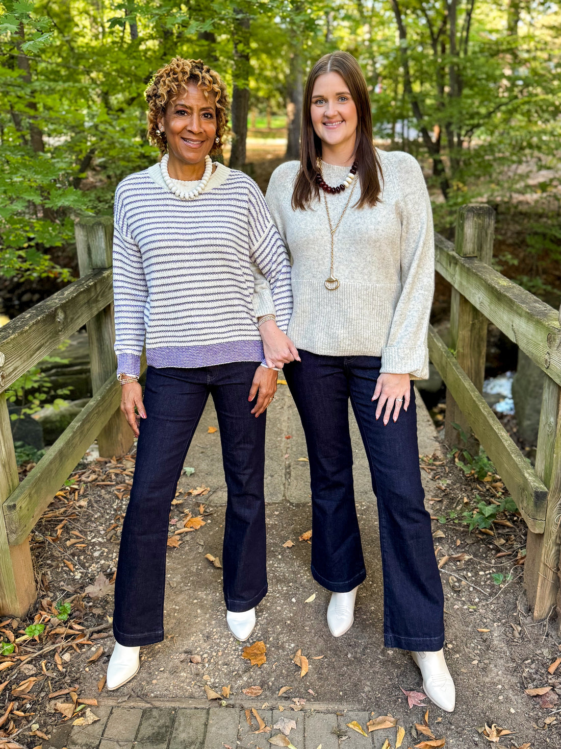 Front view of two women wearing Swagger Boutique’s Cream &amp; Purple Striped Sweater and Heathered Oatmeal Cuffed Sleeve Sweater with jeans standing on a bridge outside.