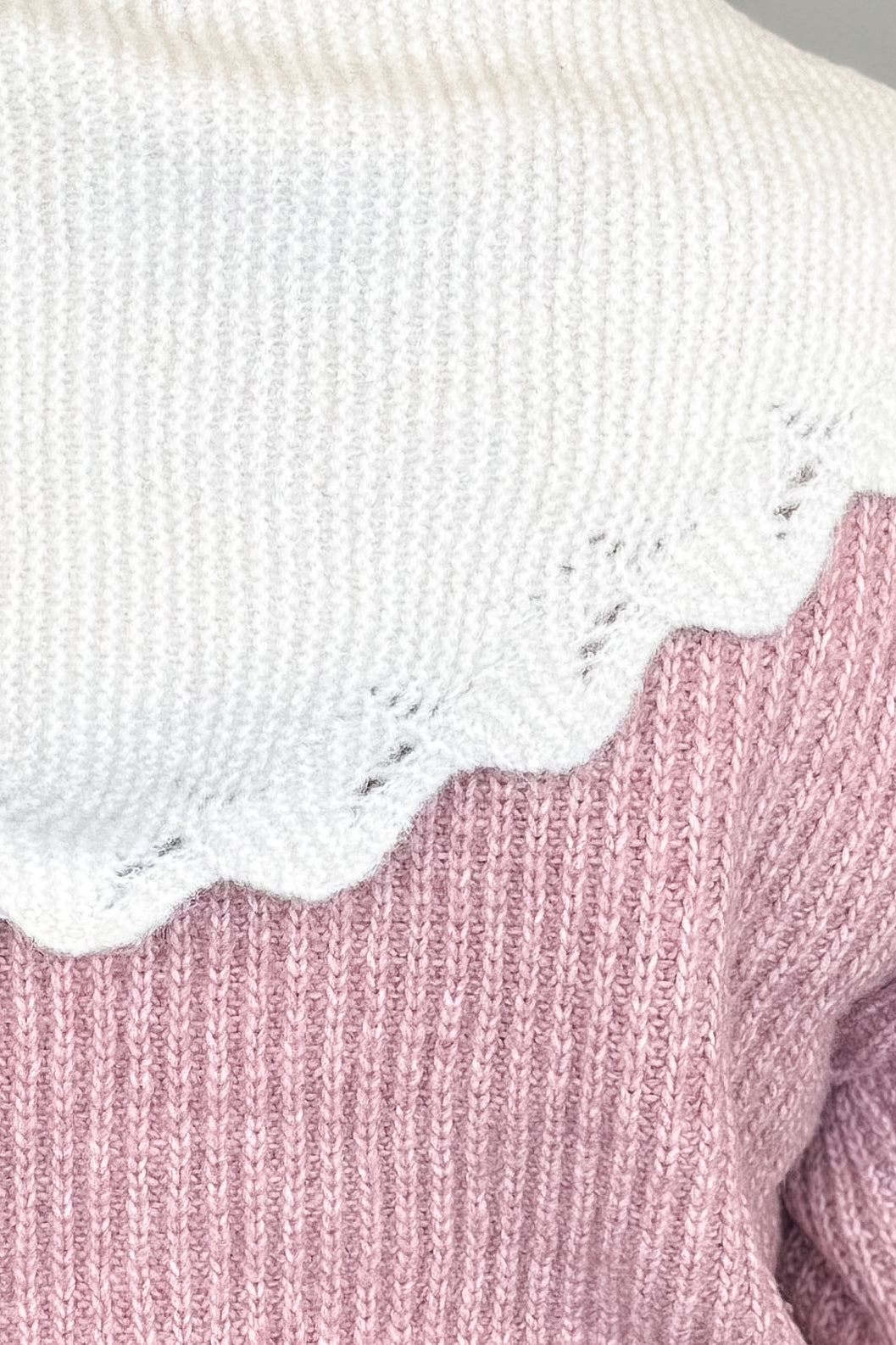 Close-up of a pink ribbed knit sweater with a contrasting white scalloped knit scarf