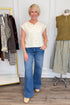 Front view of woman wearing Swagger Boutique’s Cream Sleeveless Button Up Sweater with Maya Denim Jeans by Kut from the Kloth with clothing hanging in the background.